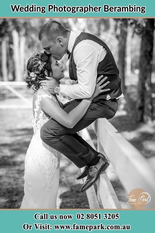 The Groom on the fence kissing her Bride at her forehead Berambing NSW 2758