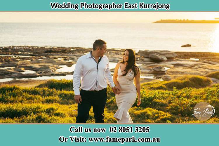 Photo of the Groom and the Bride walking near the shore as they look at each other East Kurrajong NSW 2758